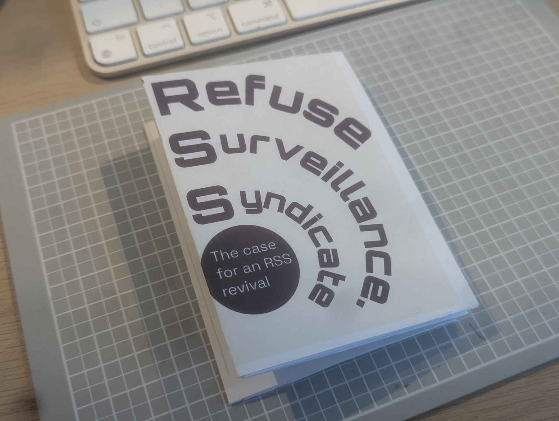 A booklet titled Refuse Surveillance Syndicate is resting on a cutting mat near a keyboard, advocating for an RSS revival.